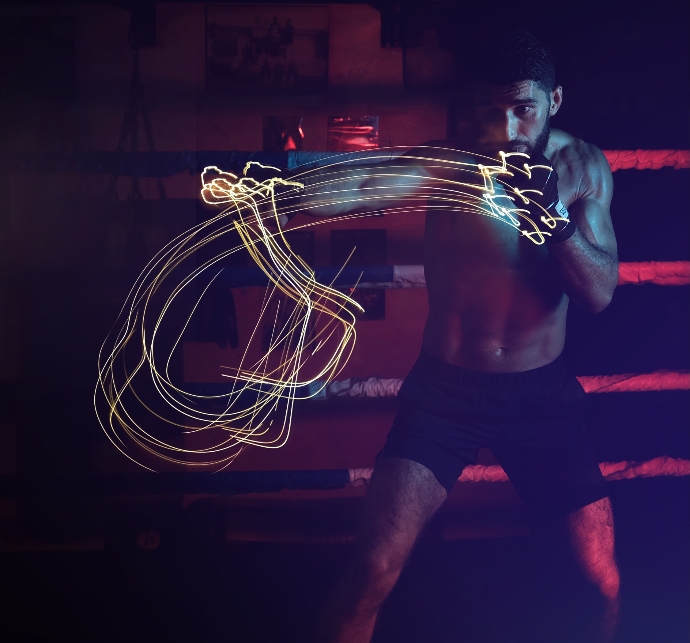 A boxer squares up in a red-lit ring, gold light trails sweeping from his gloves